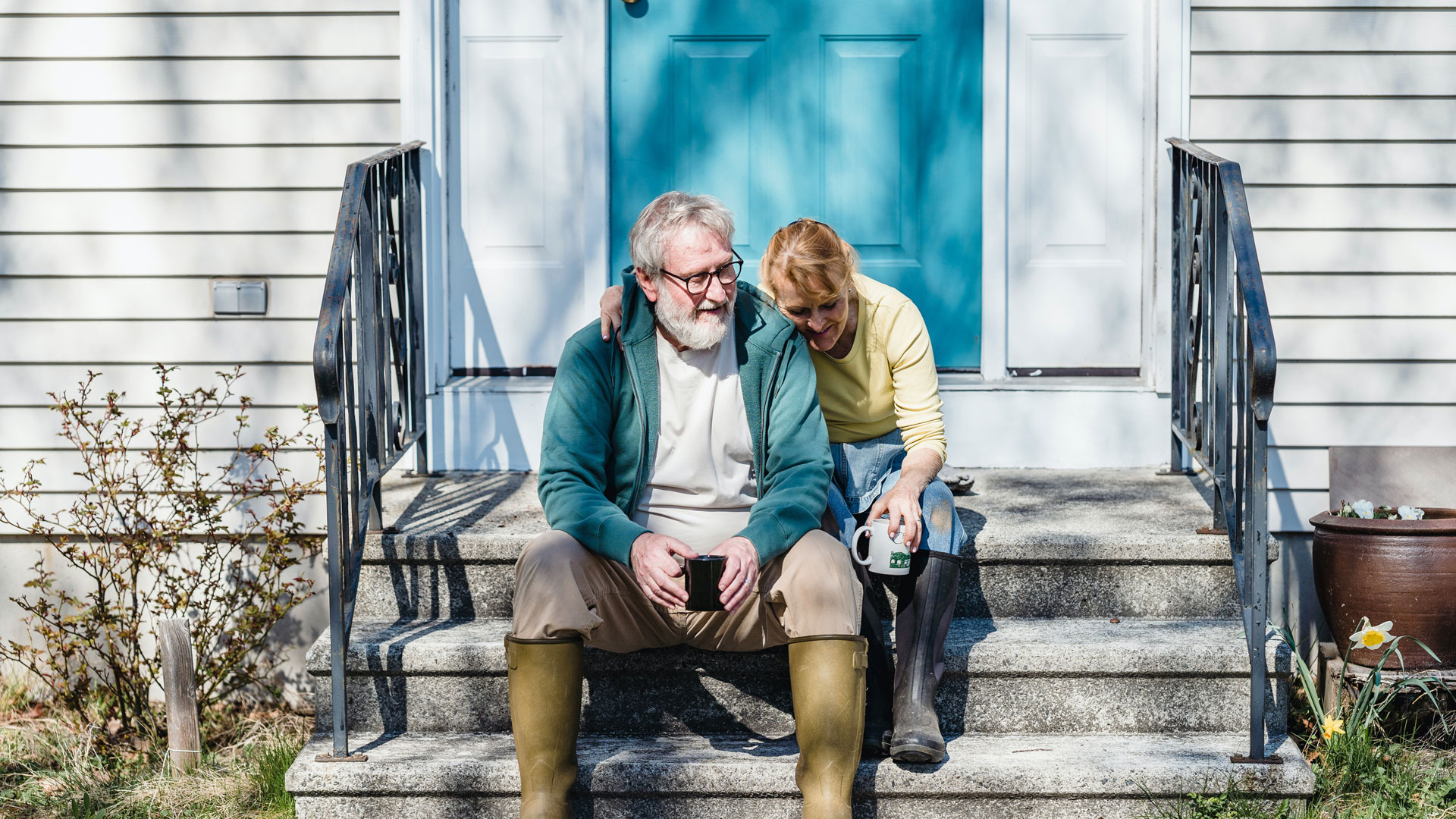 An older couple sitting on their front stoop drinking coffee together.