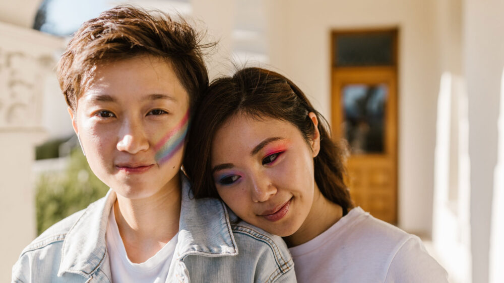 A couple with rainbow makeup in front of their home.