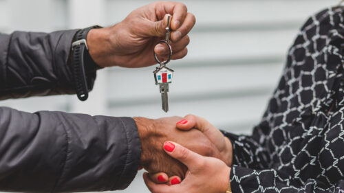 A person handing a house key to another person as they grasp hands.